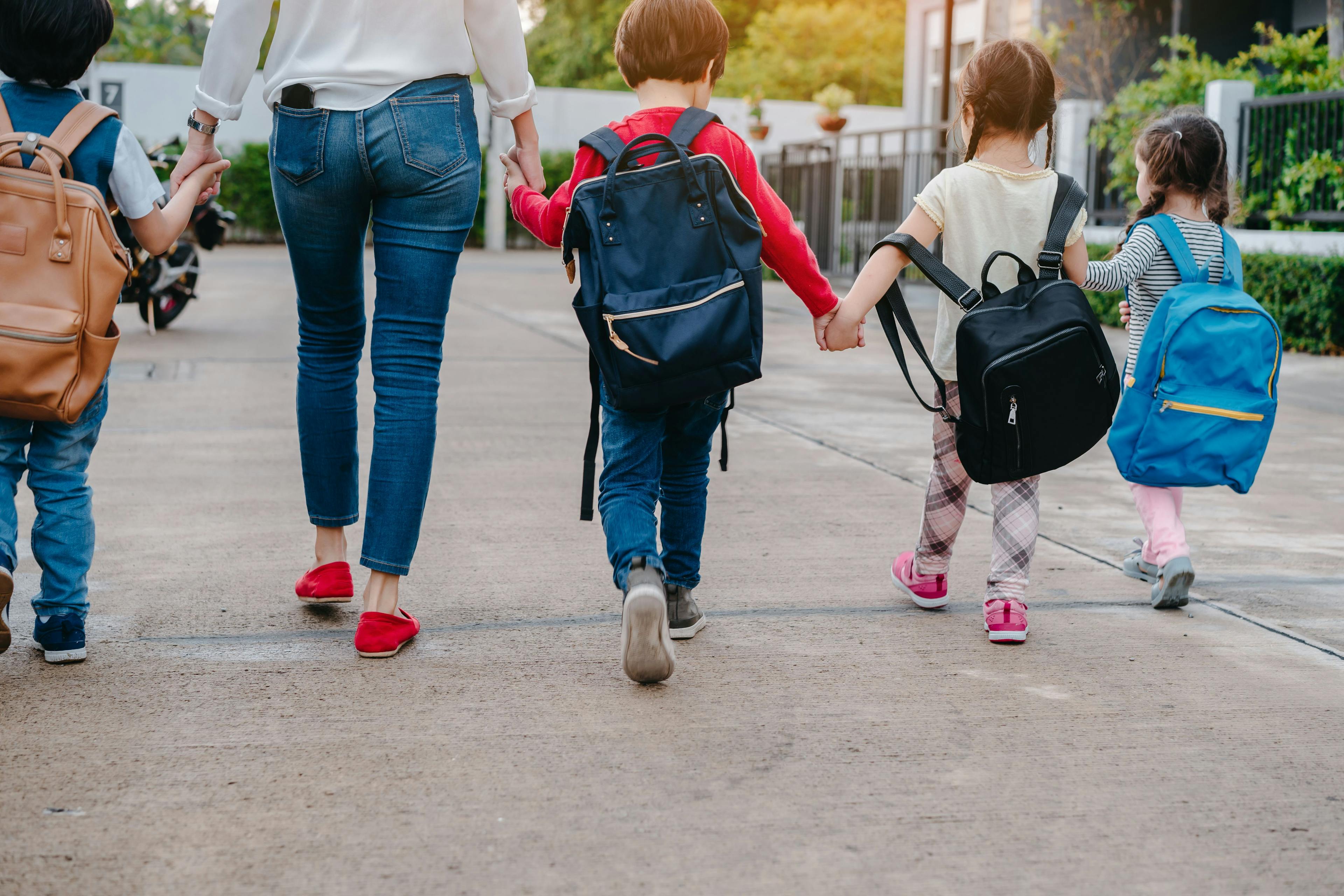 Woman and young children wearing backpacks and holding hands